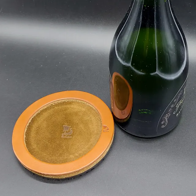 Wine bottle base, perfect to protect the table, 13cm wide-5.12 in, with a 5mm rubber base, a liquid-repellent suede leather on the inside and an 8mm cork and leather outer ring.Opplav bordbeskytter